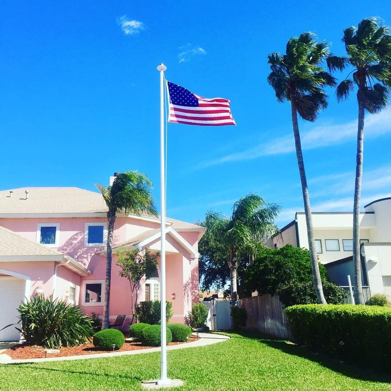 Load image into Gallery viewer, A 30-foot aluminum flagpole with an external halyard system, displaying an American flag, installed on a lawn with palm trees in the background.