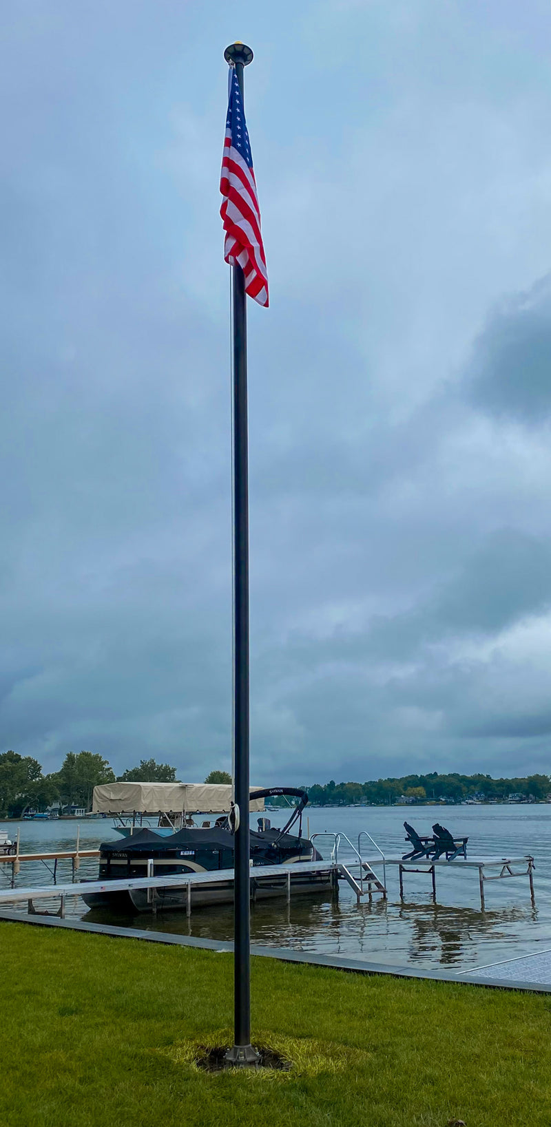 Load image into Gallery viewer, A tall aluminum flagpole with a US flag at the top, situated near a body of water and a dock.