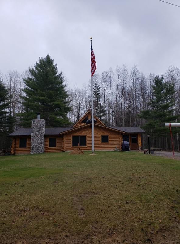 Load image into Gallery viewer, A 40-foot Lincoln Series External Halyard Aluminum Flagpole, with an American flag raised on it, standing in front of a wooden cabin.