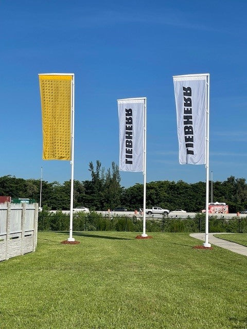 Load image into Gallery viewer, Three white fiberglass banner poles installed in a grassy commercial area, flying tall vertical banners next to a highway.