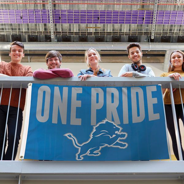 Load image into Gallery viewer, Detroit Lions Slogan Flag displayed by five young fans on a balcony, showcasing the "ONE PRIDE" message and lion logo in a vibrant lifestyle setting.