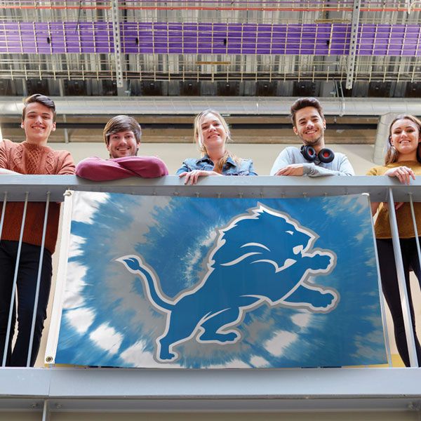 Load image into Gallery viewer, Detroit Lions Tie Dye Flag displayed on a balcony railing, held by five young fans, showcasing the unique blue, grey, and white swirl design in a lifestyle setting.