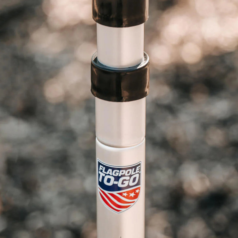 Load image into Gallery viewer, Close-up view of the gray Flagpole-To-Go Portable Telescoping Aluminum Flagpole, highlighting the mechanism where two sections meet, showing the black locking collar and the Flagpole-To-Go logo sticker.