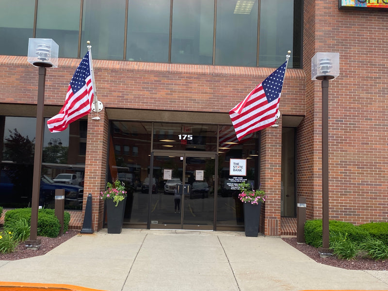 Load image into Gallery viewer, Two American flags displayed outside a brick building using the Franklin Series Outrigger Wall Mount Flagpole Set.