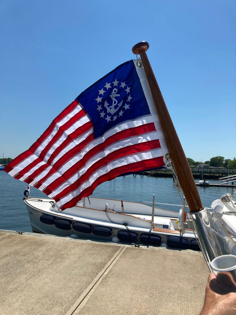 Load image into Gallery viewer, U.S. Yacht Ensign Flag with 13 stripes and a fouled anchor in the canton, displayed from a flagpole on a dock.
