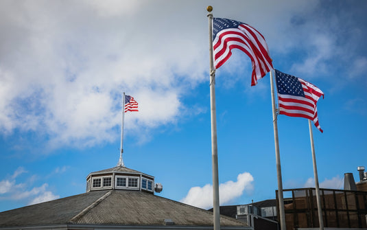 Two tall Washington Series Aluminum Flagpoles (20-25 ft.) flying American flags next to a building roof under a cloudy sky.