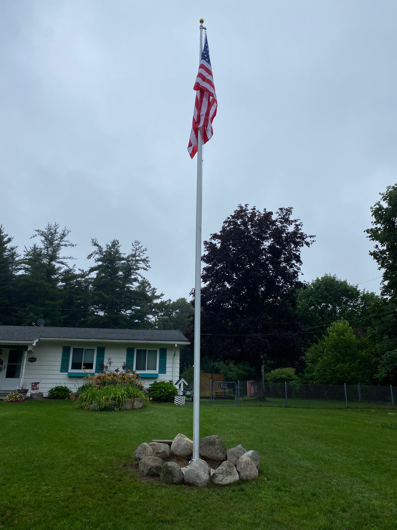 Load image into Gallery viewer, A 20-foot Lincoln Series External Halyard Aluminum Flagpole with an American flag raised on it, set on a residential lawn.

