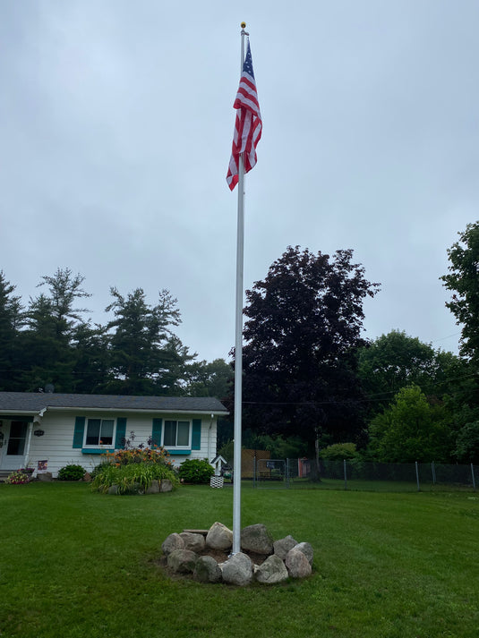 A 20-foot Lincoln Series External Halyard Aluminum Flagpole with an American flag raised on it, set on a residential lawn.