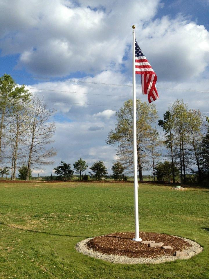 Load image into Gallery viewer, An external halyard aluminum flagpole, 25 feet tall, installed in a grassy area with a clear blue sky and some clouds in the background. An American flag is displayed at the top of the flagpole.
