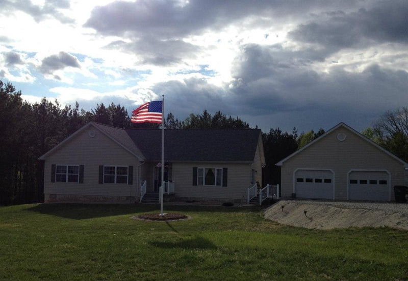 Load image into Gallery viewer, A 45-foot tall aluminum flagpole with an external halyard system, displaying an American flag, installed in front of a house.

