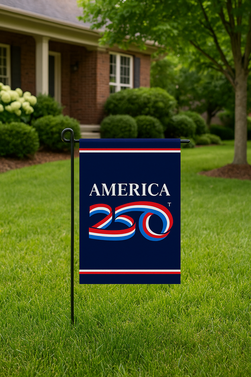 Load image into Gallery viewer, America 250 garden flag mounted on a black metal stand in a neatly trimmed front yard, with a brick house and green trees in the background.
