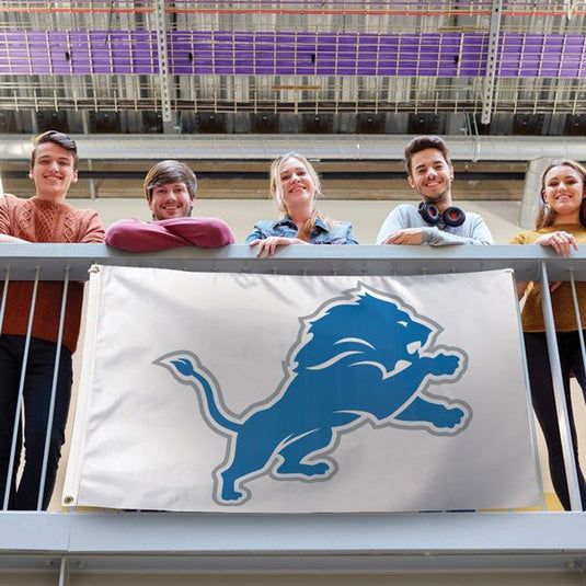 Detroit Lions Silver Background Flag displayed on a railing with five young fans smiling behind it, showing the flag's large size and vibrant blue and silver logo.
