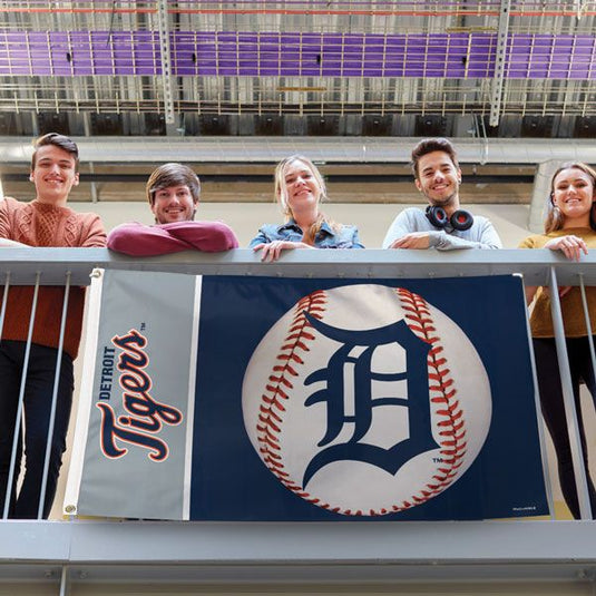 Detroit Tigers Baseball Design Flag displayed on a railing by five smiling fans, showcasing the navy blue and grey design in a vibrant lifestyle setting.