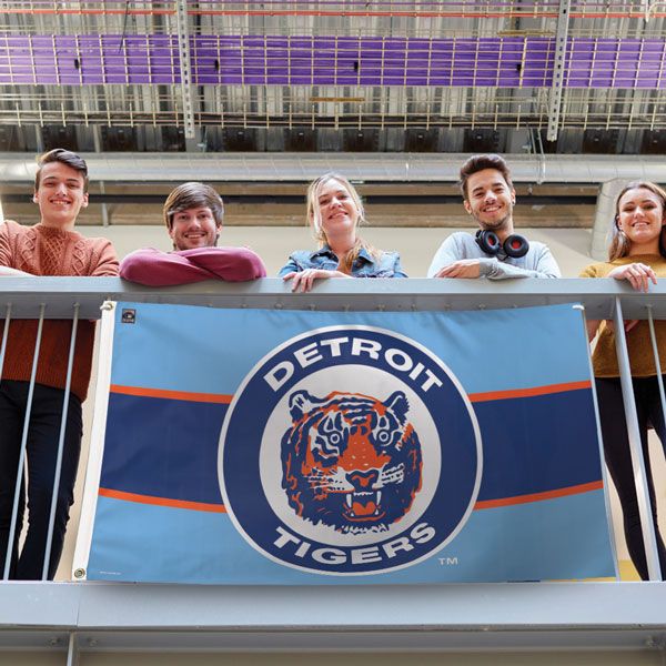Load image into Gallery viewer, Detroit Tigers Cooperstown Flag displayed on a railing by five young fans, showcasing the vintage tiger logo and the light blue and orange color scheme in a lifestyle setting.
