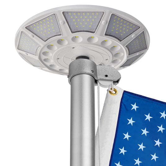 Close-up of the Elite Deluxe Solar Disk Light installed on a silver flagpole with an American flag, highlighting LED panels and mounting bracket.