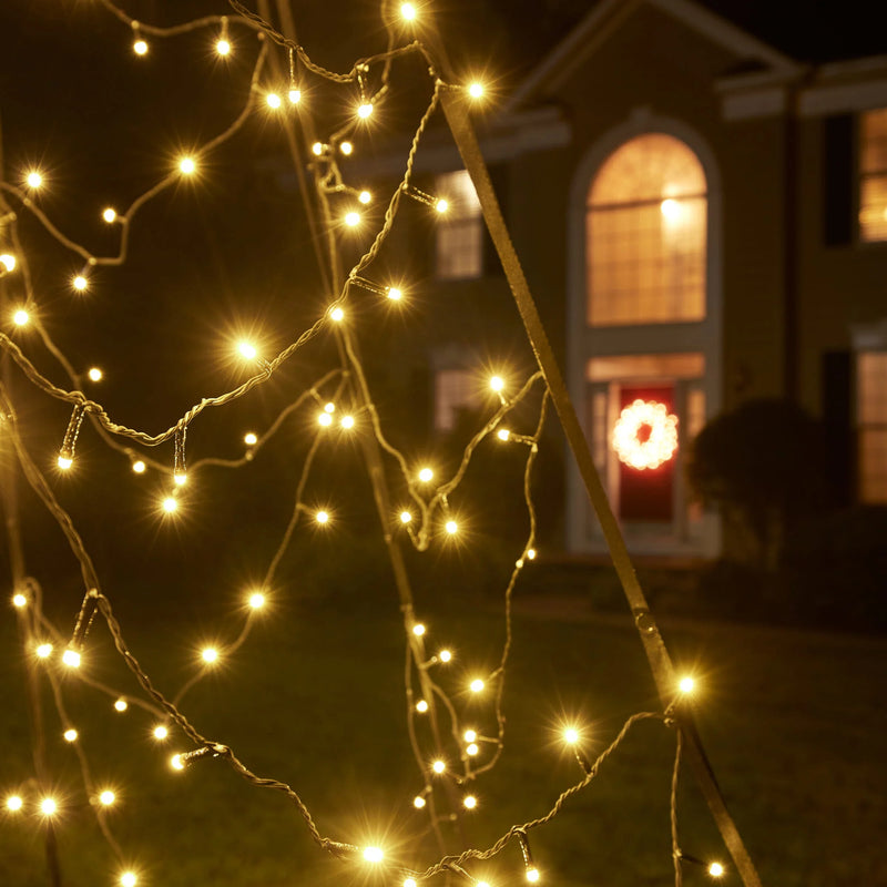 Load image into Gallery viewer, Close-up of the twinkling Fairybell Luminous Switch Flagpole Christmas Tree Light in warm white, with a house visible in the background.
