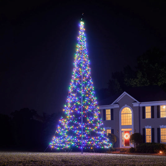 Tall, brightly lit Fairybell Multi-Color Flagpole Christmas Tree Light providing wide-angle illumination to a residential landscape at night.