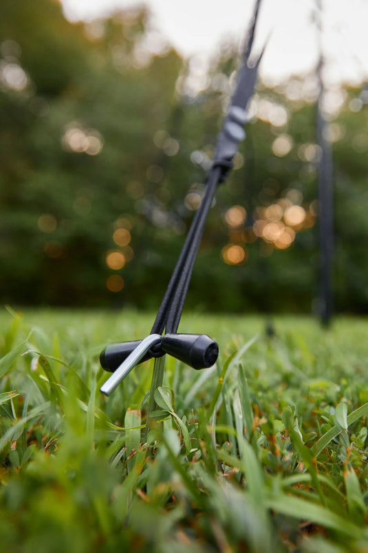 Close-up of the black tether and ground stake securing the Fairybell Single Color Flagpole Christmas Tree Light base in the grass.