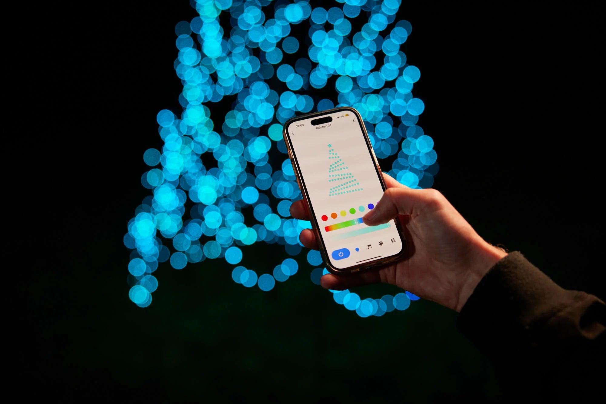 Hand using the color picker in the control app for the Fairybell Smart Magic Light against a background of blue bokeh lights.