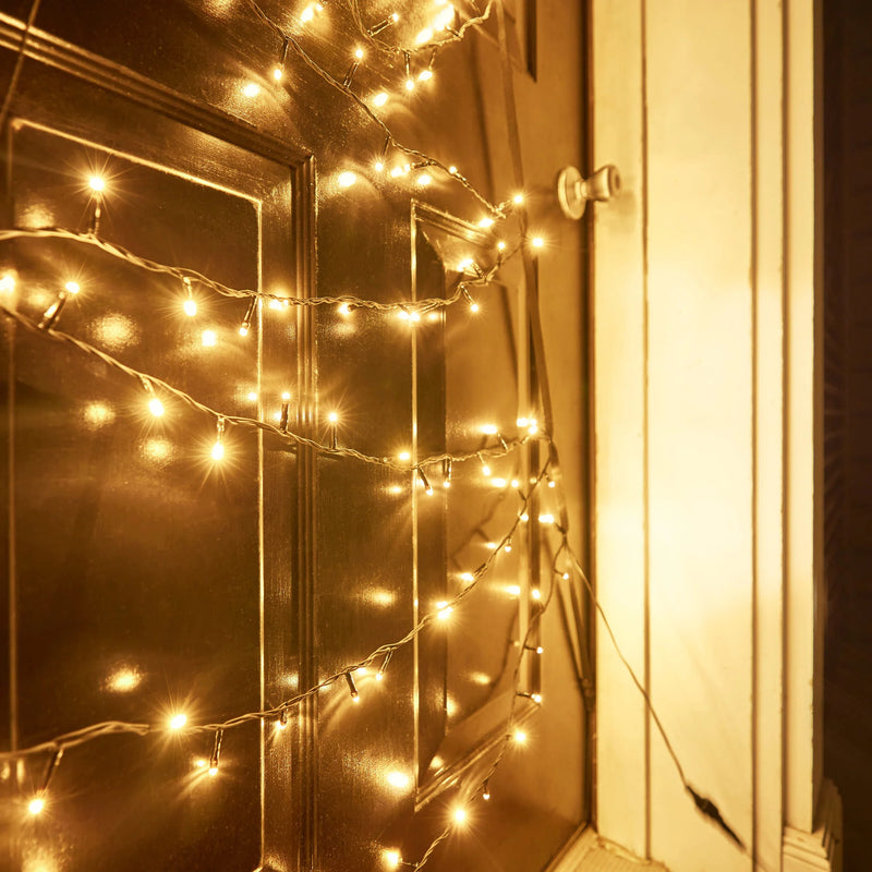 Load image into Gallery viewer, Close-up of Fairybell warm white LED Christmas tree lights arranged on a door, showing glowing bulbs and wiring detail.
