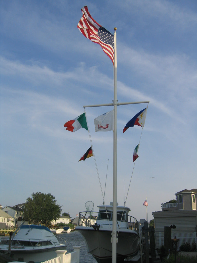Load image into Gallery viewer, Fiberglass external halyard flagpole with yardarm installed by the waterfront, flying the U.S. flag and nautical flags near docked boats.
