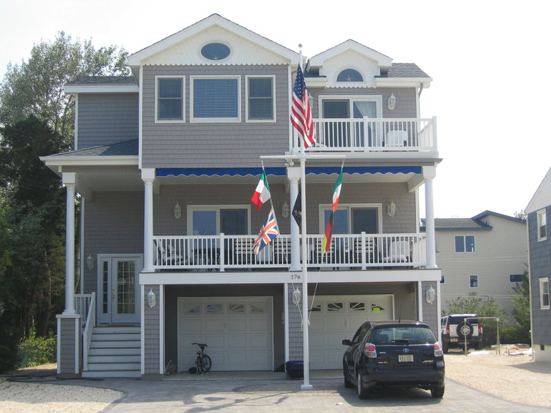 Load image into Gallery viewer, Fiberglass external halyard flagpole with yardarm mounted in front of a coastal home, displaying multiple national flags and the American flag.
