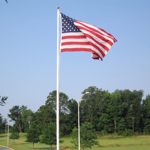 Fiberglass external hinge base flagpole standing in a grassy landscape, flying the American flag on a clear blue day.