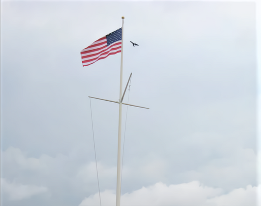 Tall, white Fiberglass Flagpole flying the American flag at half-mast from the upper main line. Below the flag, a horizontal Fiberglass Gaff crossbar is attached, simulating a ship's mast, used for flying multiple flags or nautical pennants.