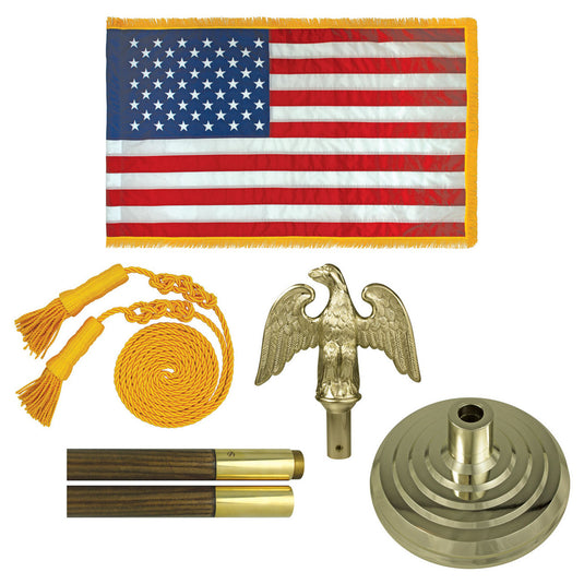 Lay-flat view of all components in the Freedom Indoor Flag Set. The parts include the fringed US flag, the coiled gold cord with tassels, the gold eagle finial, the tiered gold floor stand base, and two sections of the wood-grained flagpole with brass ferrules.