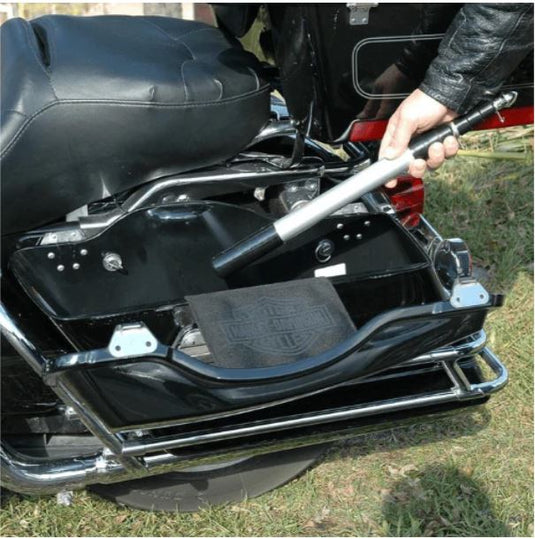 A person demonstrating the portability of the Hide-A-Pole, shown placing the compact, collapsed flagpole into a black motorcycle saddlebag for easy storage and travel. The image highlights the product's intended discreet, portable nature.