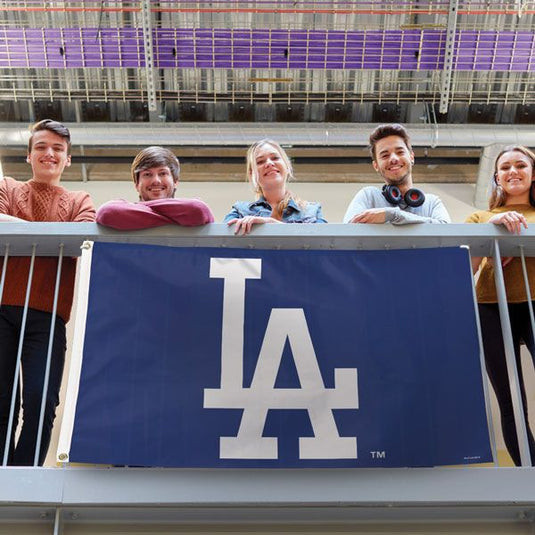 A group of fans displaying a Los Angeles Dodgers flag with the LA logo from a balcony.