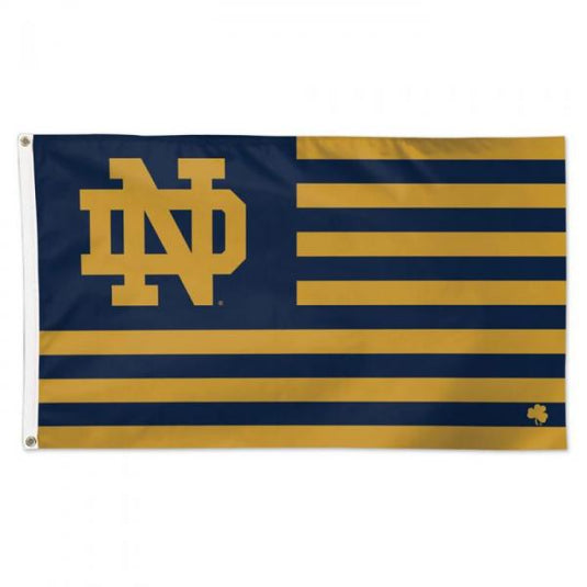 Notre Dame Fighting Irish flag with gold ND logo on a navy and gold striped background, small shamrock in bottom right corner.