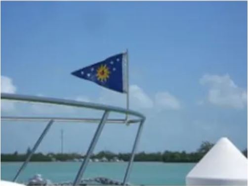 Load image into Gallery viewer, Small blue burgee flag, featuring a yellow sun and white stars, flying from the Original Swiveler Boat Flagpole mounted on a sailboat railing against a bright blue sky.
