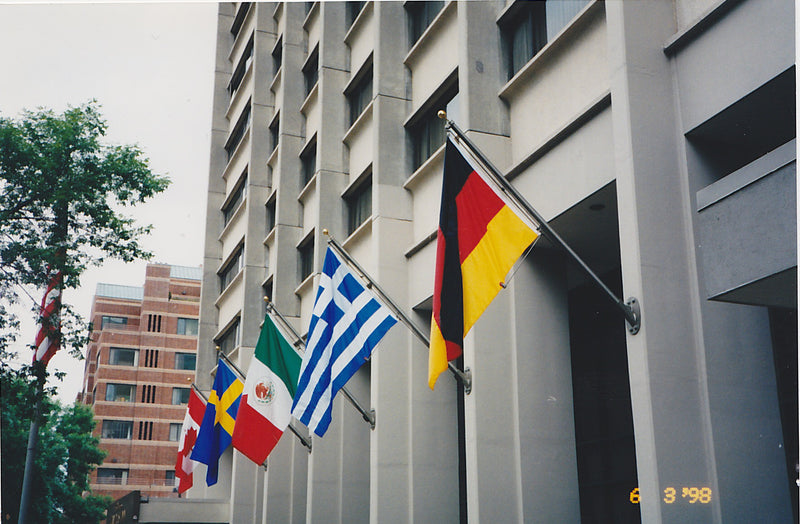 Load image into Gallery viewer, Multiple international flags (Germany, Greece, Mexico, Sweden, Canada) displayed from 15 ft. Outrigger Wall Mount Flagpoles (4-inch butt diameter) on a tall commercial building.
