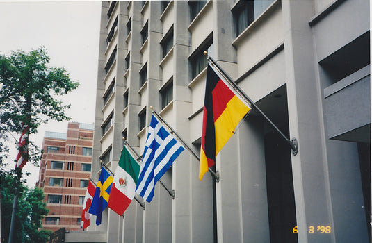 Multiple international flags (Germany, Greece, Mexico, Sweden, Canada) displayed from 15 ft. Outrigger Wall Mount Flagpoles (4-inch butt diameter) on a tall commercial building.