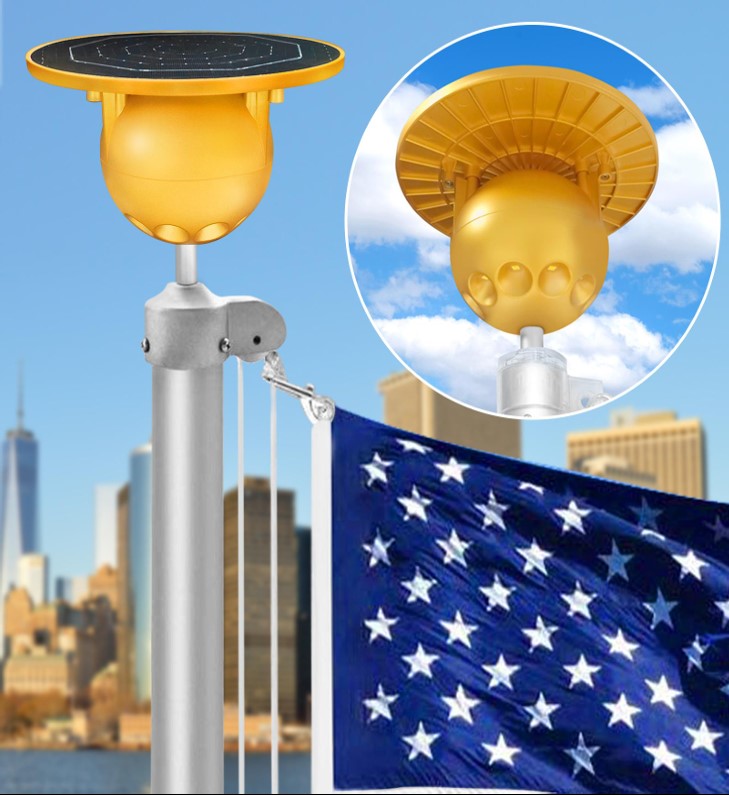 Load image into Gallery viewer, Gold Solar Flagpole Ball Light mounted atop a pole with an American flag flying below it and a cityscape background.
