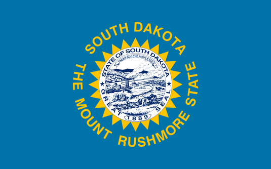 South Dakota state flag with the state seal centered on a sky-blue field, surrounded by a gold sun and the words “South Dakota – The Mount Rushmore State.”