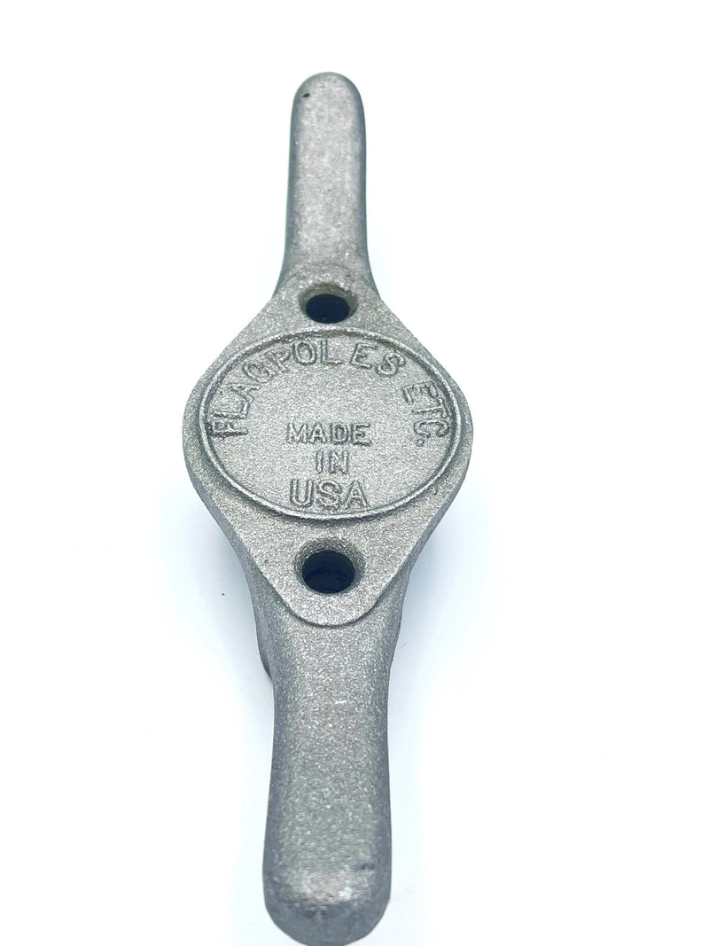 Load image into Gallery viewer, High-angle view of the Heavy Duty Cast Aluminum Flagpole Cleat in a light silver-grey finish. The rugged metal cleat features a raised central oval containing the embossed "MADE IN USA" text, ensuring durability for outdoor flagpole use.
