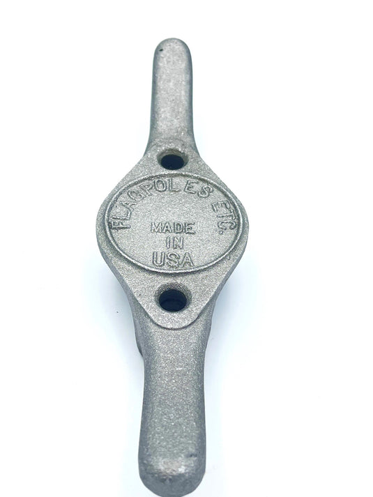 High-angle view of the Heavy Duty Cast Aluminum Flagpole Cleat in a light silver-grey finish. The rugged metal cleat features a raised central oval containing the embossed 