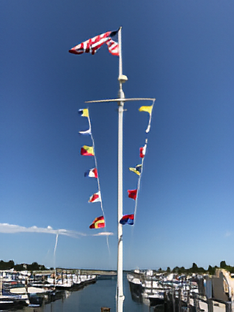 A 20-foot nautical single mast flagpole with a yardarm, featuring a series of colorful flags, installed over a marina filled with boats, under a clear blue sky.